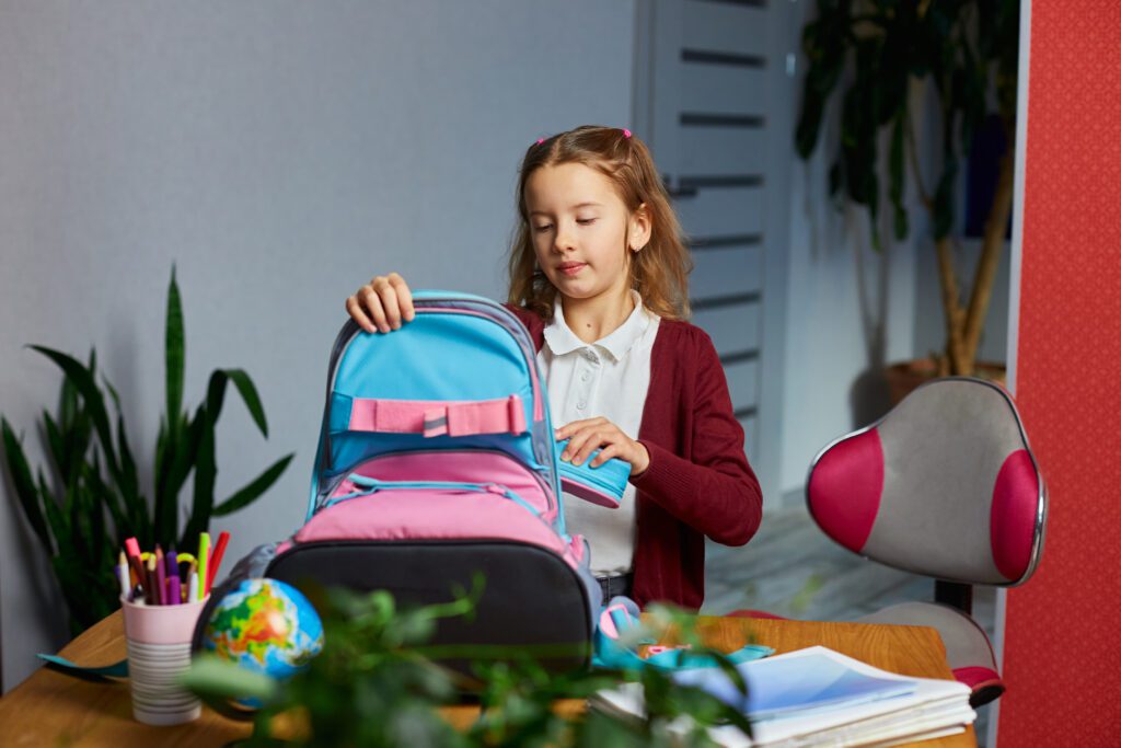 Uczennica pakuje się do szkoły. Na jej biurku znajdują się długopisy i mały globus. Techniki uczenia się dla dzieci.